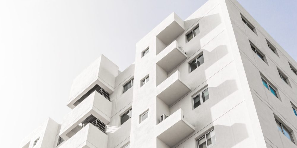 foto-de-baixo-angulo-da-fachada-de-um-edificio-moderno-branco-sob-um-ceu-azul-claro-scaled